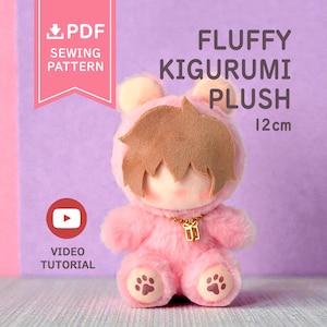 May include: A pink fluffy kigurumi plush toy with brown hair, rounded ears, and paw prints on the feet. A gold-colored chain with a small gift charm hangs around the neck. Text on the image reads PDF SEWING PATTERN, FLUFFY KIGURUMI PLUSH 12cm, and VIDEO TUTORIAL.