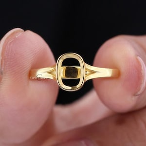 May include: A gold ring featuring a central oval-shaped setting with a black inlay. The band has a split-shank design that tapers toward the back. The text Carat Culture is visible in small print on the side of the ring and at the bottom left.