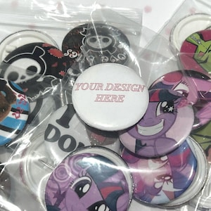 May include: A collection of circular pin-back buttons packaged in individual clear plastic bags. The buttons feature various colorful graphic illustrations, including cartoon characters and a white button with the text YOUR DESIGN HERE.