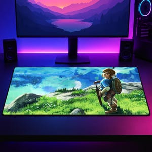 May include: A rectangular desk mat featuring a vibrant, high-resolution illustration of a character with blonde hair, wearing a blue tunic and carrying a sword and shield, standing on a grassy cliff overlooking a vast, bright blue landscape.