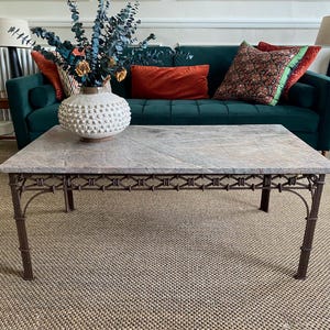 May include: A rectangular coffee table featuring a polished grey marble top with natural veining and a dark brown metal base. The base is constructed with four slender legs and a decorative lattice apron design connecting the legs underneath the top.