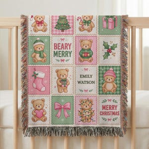 Könnte beinhalten: Eine gewebte Wohndecke mit einem Gitter aus weihnachtlichen Quadraten mit Teddybären, einem geschmückten Baum, einem rosa Geschenk, einem Strumpf, Stechpalmen und Schleifen. Der Text lautet BEARY MERRY, EMILY WATSON und MERRY CHRISTMAS. Mit Fransen.