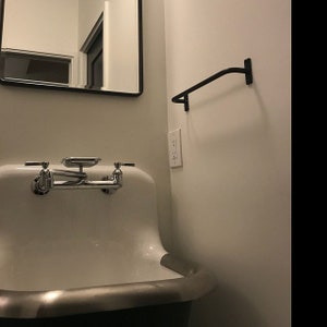 May include: A white porcelain sink with a chrome faucet and a black metal towel bar mounted on the wall. The sink is in a bathroom with a white tiled wall and a mirror.
