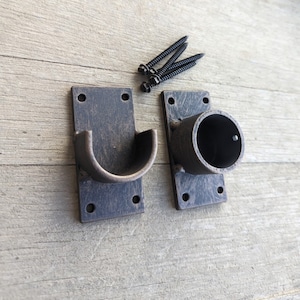 May include: Two black metal curtain rod brackets with screws. One bracket has a curved end for holding a curtain rod, and the other has a round opening for a rod.