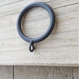May include: Black metal curtain ring with a small loop at the bottom. The ring is approximately 5 cm in diameter.