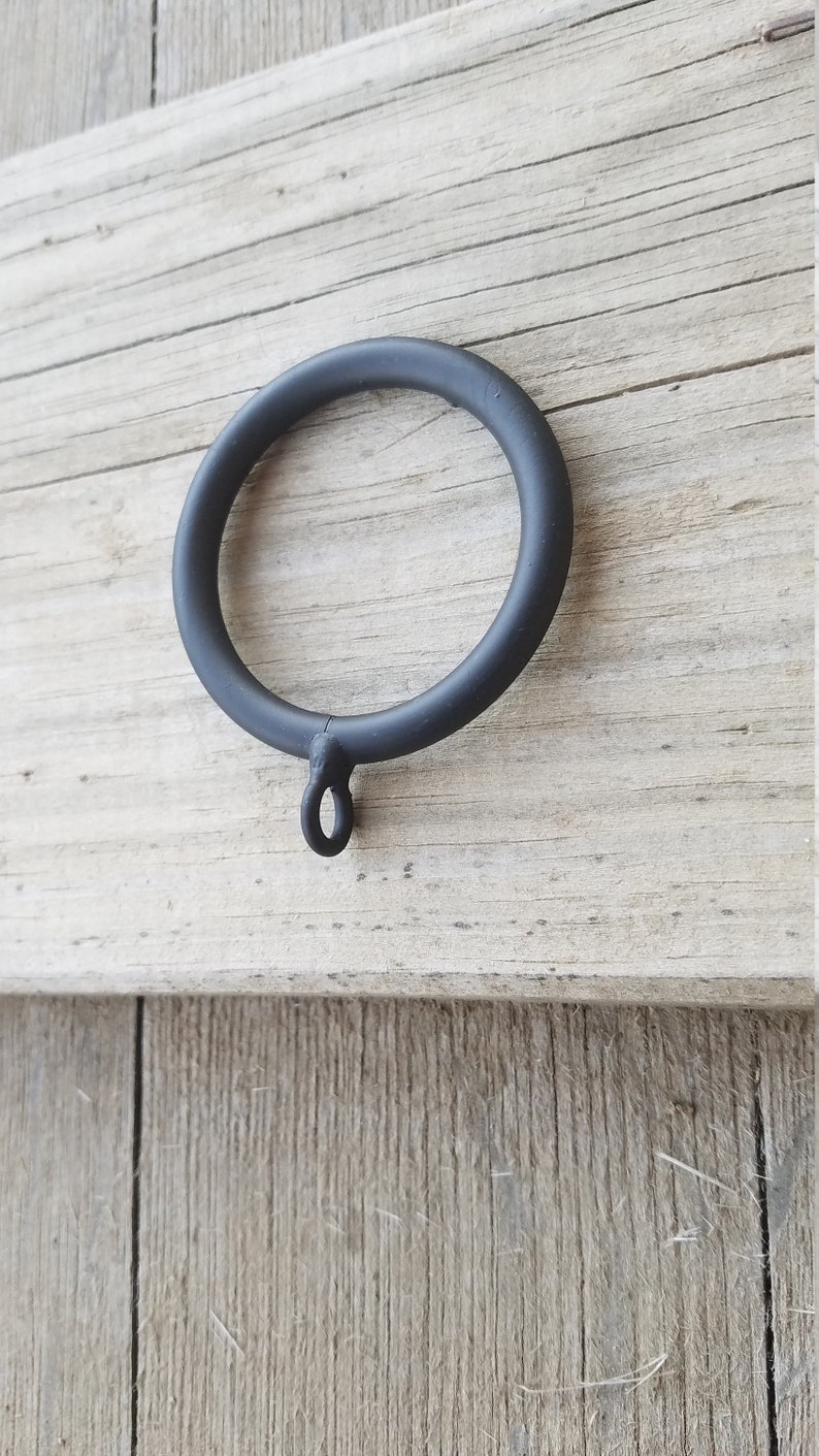 May include: Black metal curtain ring with a small loop at the bottom. The ring is approximately 5 cm in diameter.