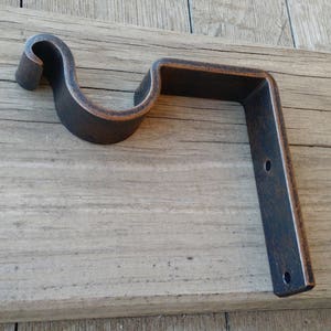 May include: A rustic metal bracket with a curved arm, perfect for hanging curtains or other decorative items. The bracket is made of dark brown metal with a distressed finish.