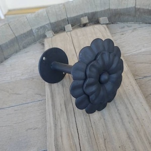 May include: Black metal curtain rod finial with a flower design. The finial is attached to a metal rod.