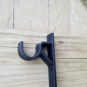 May include: Black metal curtain rod bracket mounted on a wooden surface.