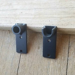 May include: Two black metal wall mounts for hanging items. One mount has a round opening and the other has a curved opening.