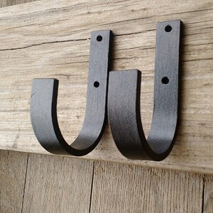 May include: Two black metal hooks with a curved design are mounted on a wooden surface.