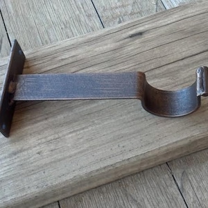 May include: A metal curtain rod bracket with a rustic finish. The bracket is designed to hold a curtain rod and is attached to a wall or ceiling.