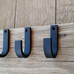 May include: Four black metal hooks mounted on a wooden surface. The hooks are in a row and are all facing the same direction. They are made of a sturdy metal and have a simple, classic design.