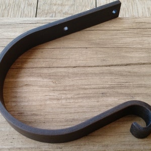 May include: A dark brown metal hook with a curved design. The hook is mounted on a wooden surface.