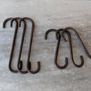 May include: A collection of six dark brown metal S-hooks. The hooks are arranged in two groups, with three hooks in each group. The hooks have a rustic, aged appearance, suggesting they are vintage or have been treated to look old.
