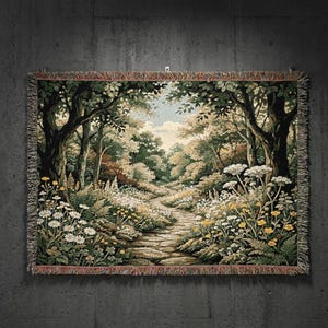 May include: A rectangular woven tapestry blanket featuring a detailed forest scene with a stone path winding through trees, lush green foliage, and clusters of white and yellow wildflowers. The edges are finished with a decorative fringe border.