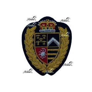 Pode incluir: Um emblema bordado azul-escuro com um escudo central dividido em quatro quadrantes com detalhes em fios dourados, vermelhos e prateados. O escudo é encimado por uma coroa detalhada e rodeado por uma borda de coroa de louros dourada.