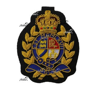May include: A black embroidered patch featuring a gold crown at the top, a central circular crest with red, blue, and white sections, and gold laurel leaves on the sides. The crest includes the Roman numerals MCMLXVII and a blue ribbon banner.