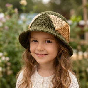 May include: A crochet bucket hat featuring a geometric color-blocked design. The hat is constructed with dark olive green, cream, and tan yarn, showcasing a structured crown and a downward-sloping brim with a dense, uniform stitch pattern.