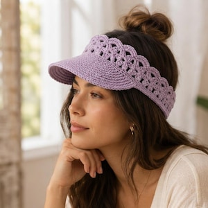 May include: A light purple crochet visor featuring a solid brim and a decorative scalloped, open-work band that wraps around the head. The accessory is crafted from yarn with a consistent stitch pattern, providing a textured appearance.