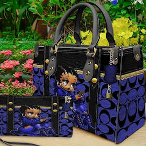 May include: A structured handbag and matching rectangular wallet featuring a black and blue patterned exterior with a repeating logo design. Both items display a graphic of a cartoon character with dark hair and blue clothing, accented by gold-tone hardware, black leather-like trim, and a small hanging padlock charm.