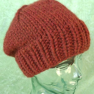 May include: A rust-colored knitted beanie hat. The hat is made of a thick yarn and has a slouchy fit.