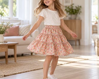 Può includere: Una t-shirt bianca a maniche corte abbinata a una gonna a balze con un colorato motivo floreale nei toni del rosa, arancione e giallo. La gonna presenta un elastico in vita e una silhouette svasata, completata da semplici sneakers bianche.