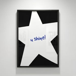 Può includere: Una stampa artistica da parete incorniciata che presenta una grande stella bianca a cinque punte su uno sfondo nero a tinta unita. Al centro della stella bianca si trova il testo "u shine!" scritto in un semplice carattere blu scuro, stile manoscritto.