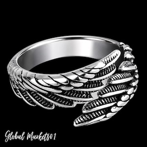 May include: A silver-toned metal ring featuring a wrap-around design that resembles a pair of feathered wings. The surface of the ring has a polished finish with darkened recessed areas to highlight the detailed texture of the individual feathers.