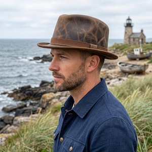 May include: A brown leather fedora hat with a distressed, marbled texture and a smooth, solid brown leather band around the base. The hat features a structured crown and a medium-width brim, showcasing a weathered appearance with dark brown tones.