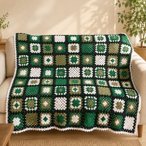 May include: A handmade crochet blanket featuring a grid of square motifs in shades of forest green, olive green, and white. The squares are joined by a black yarn border, and the entire blanket is finished with a white scalloped crochet edge.