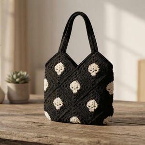 May include: A black crochet tote bag featuring a repeating diamond pattern with white skull motifs centered in each square. The bag has two integrated black handles and is constructed from yarn with a visible textured stitch throughout the design.