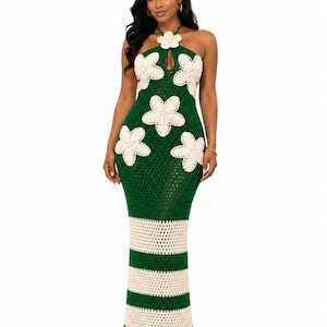 Könnte beinhalten: Ein bodenlanges, dunkelgrünes Häkel-Maxikleid mit Neckholder-Ausschnitt und einer großen cremefarbenen Blumenapplikation. Das Oberteil ist mit weiteren cremefarbenen Blumenmotiven verziert, während der untere Teil horizontale cremefarbene Streifen aufweist.