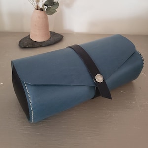 May include: A blue leather roll-up case with a black strap and a silver button closure.