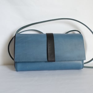 May include: A blue leather crossbody bag with a black strap and the word "SENATI" embossed on the front.