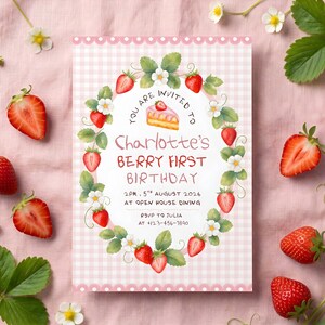 Puede incluir: Una tarjeta de invitaci&oacute;n rectangular con un borde de cuadros rosa claro y blanco que presenta una corona ovalada central de fresas, hojas verdes y flores blancas. El texto dice: You are invited to Charlotte's Berry First Birthday.