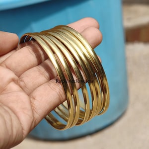 Peut inclure: Un ensemble de plusieurs joncs en métal doré, lisses et polis, avec un profil arrondi. Le texte RaiSilverJewelers est visible sur la surface des bracelets. Ces bracelets circulaires présentent une finition métallique réfléchissante et simple.