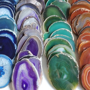 Peut inclure: Assortiment de tranches d'agate de diff&eacute;rentes couleurs, notamment bleu, violet, vert et orange. Les tranches sont empil&eacute;es et dispos&eacute;es en rang&eacute;es, mettant en valeur leurs motifs et textures naturels.