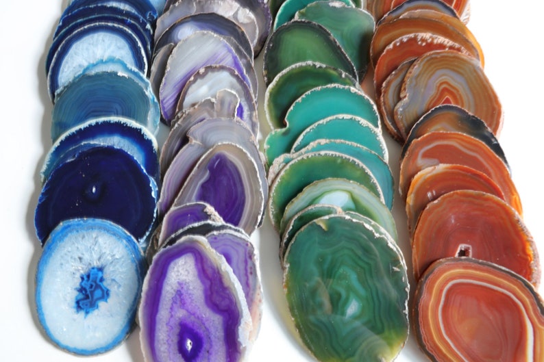 Peut inclure: Assortiment de tranches d'agate de diff&eacute;rentes couleurs, notamment bleu, violet, vert et orange. Les tranches sont empil&eacute;es et dispos&eacute;es en rang&eacute;es, mettant en valeur leurs motifs et textures naturels.