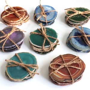 May include: Set of eight agate coasters in various colors, including green, blue, purple, and brown. Each coaster is made of natural agate and is tied with twine.