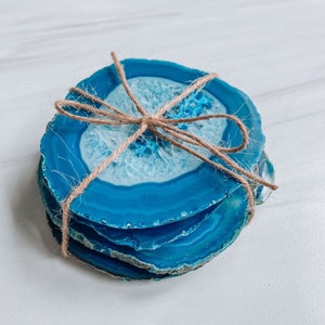 Peut inclure: Ensemble de quatre sous-verres en agate bleue li&eacute;s ensemble avec de la ficelle. Les sous-verres sont en pierre naturelle et ont une forme unique et organique.