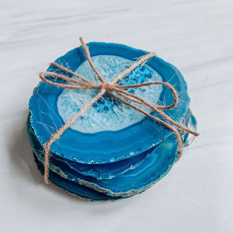 Peut inclure: Ensemble de quatre sous-verres en agate bleue li&eacute;s ensemble avec de la ficelle. Les sous-verres sont en pierre naturelle et ont une forme unique et organique.