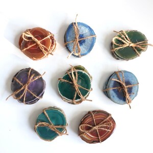 Peut inclure: Ensemble de neuf sous-verres en agate de diff&eacute;rentes couleurs, dont le violet, le vert, le bleu et le brun. Chaque sous-verre est fait d'une tranche d'agate naturelle et est li&eacute; avec de la ficelle.