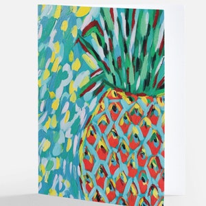 May include: Greeting card featuring a colorful painting of a pineapple. The pineapple has a red and yellow body with a blue background. The top of the pineapple has green leaves. The card is white on the right side.