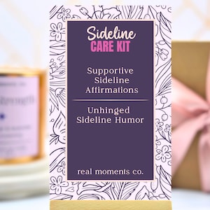May include: A rectangular card with a dark purple center and a white floral border. The text reads: Sideline CARE KIT, Supportive Sideline Affirmations, Unhinged Sideline Humor, and real moments co. The card is displayed on a light wooden base.