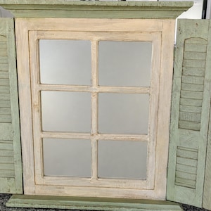 May include: A rectangular wall mirror designed to resemble a window with six panes. The frame is painted in a distressed off-white finish, while the two attached side shutters are painted in a muted sage green with horizontal slats.