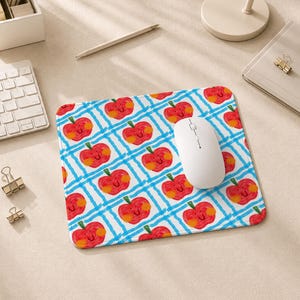 Peut inclure: Un tapis de souris carré arborant un motif répétitif de pommes rouges aux visages souriants et aux joues orange, sur un fond à quadrillage bleu clair. Une souris d'ordinateur blanche est posée sur la surface du tapis de souris.