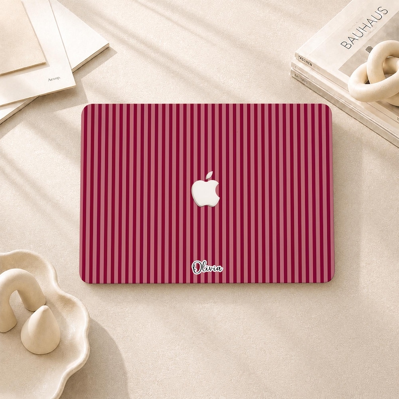 Peut inclure: Un autocollant pour ordinateur portable rectangulaire avec un motif &agrave; rayures verticales alternant des nuances de rouge fonc&eacute; et de rose clair. Le logo Apple blanc est au centre et le pr&eacute;nom Olivia est &eacute;crit en lettres cursives blanches en bas.
