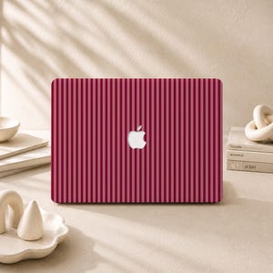 Peut inclure: Un ordinateur portable doté d'un revêtement à rayures verticales rouge foncé et rose clair sur le couvercle. Le centre du couvercle affiche un logo Apple blanc. L'ordinateur est placé horizontalement, mettant en valeur le motif uniforme.