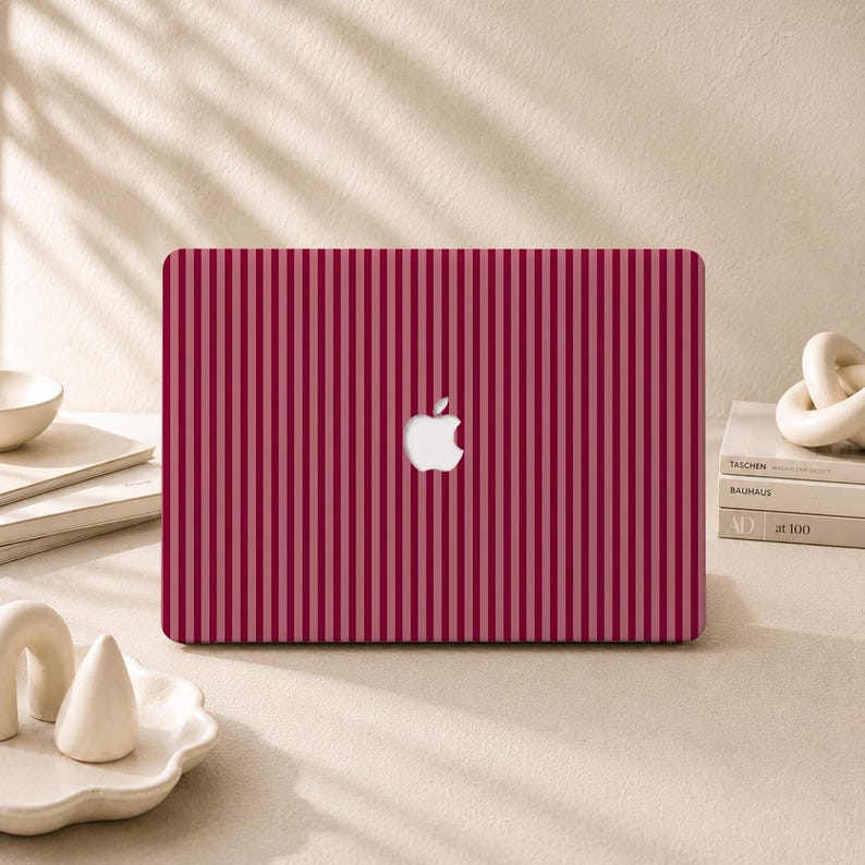 Peut inclure: Un ordinateur portable dot&eacute; d'un rev&ecirc;tement &agrave; rayures verticales rouge fonc&eacute; et rose clair sur le couvercle. Le centre du couvercle affiche un logo Apple blanc. L'ordinateur est plac&eacute; horizontalement, mettant en valeur le motif uniforme.